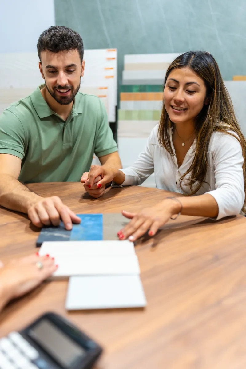 Two people lean over a table together, comparing samples, a calculator on the table beside them