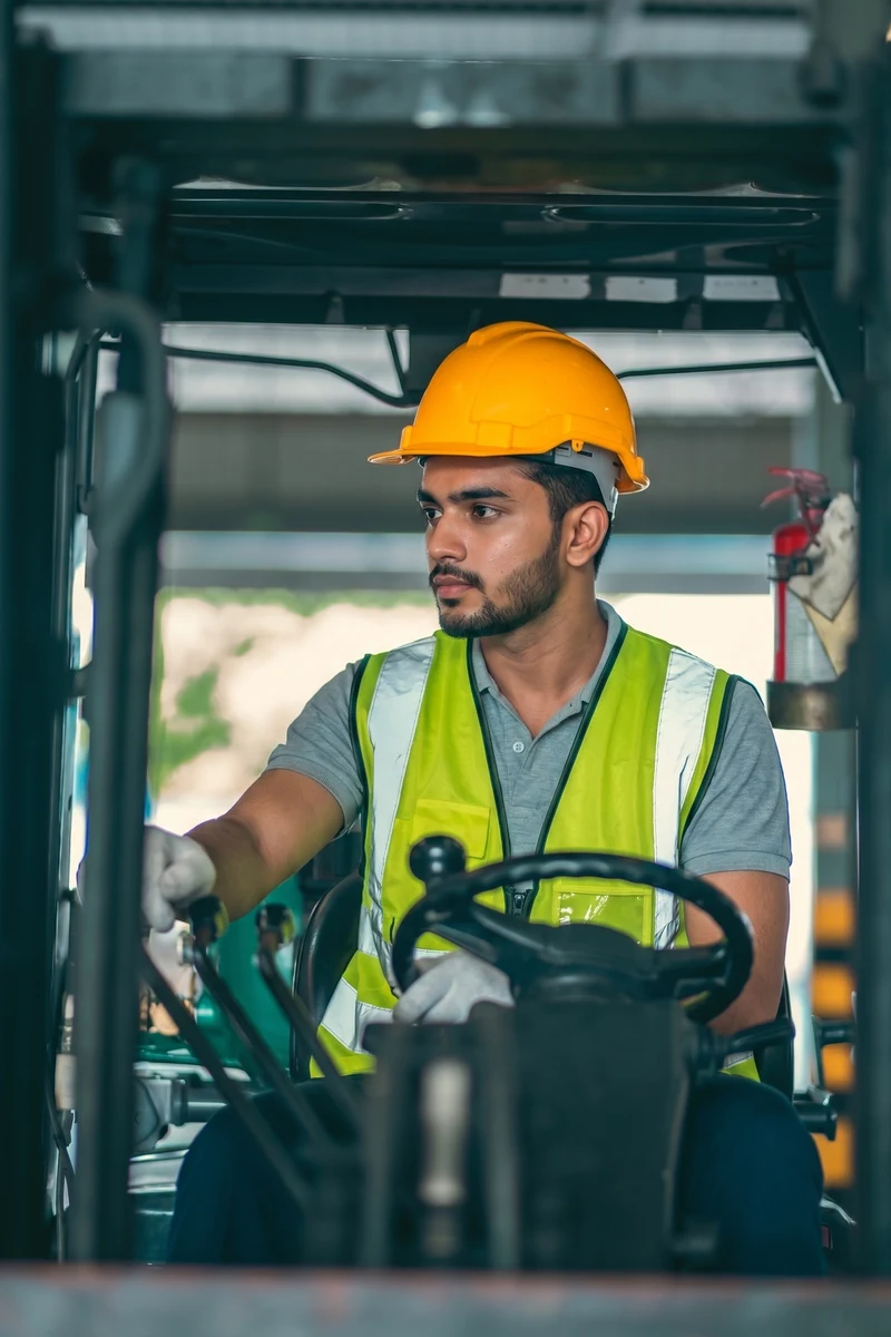 An operator in a hard hat and hi-vis vest works the controls from the cab